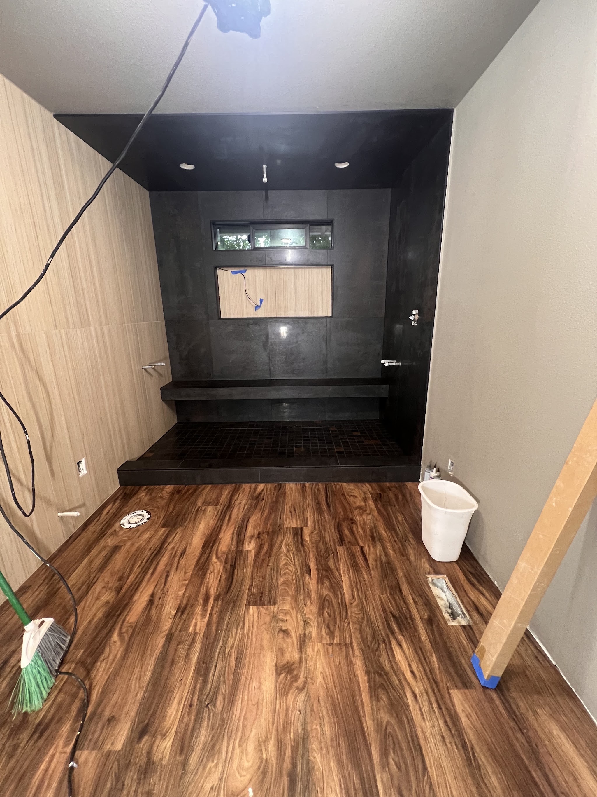 Dark modern wet room with stone bench shower and walnut LVP flooring by Castor's Flooring