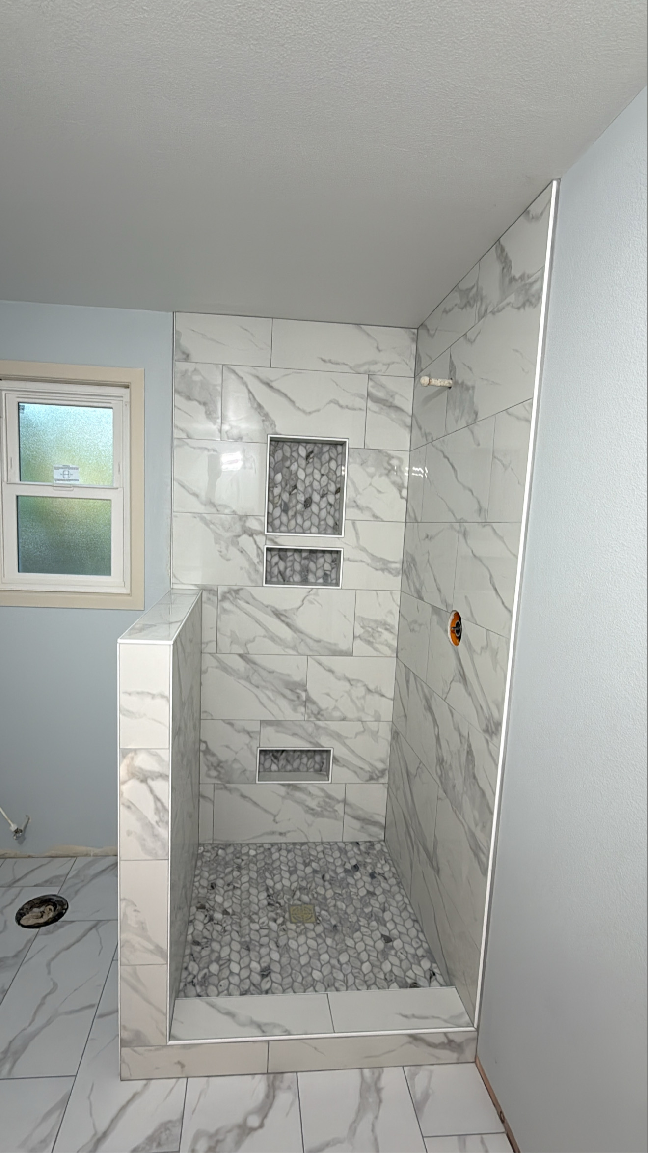 Marble-look tile shower with built-in niche shelving by Castor's Flooring