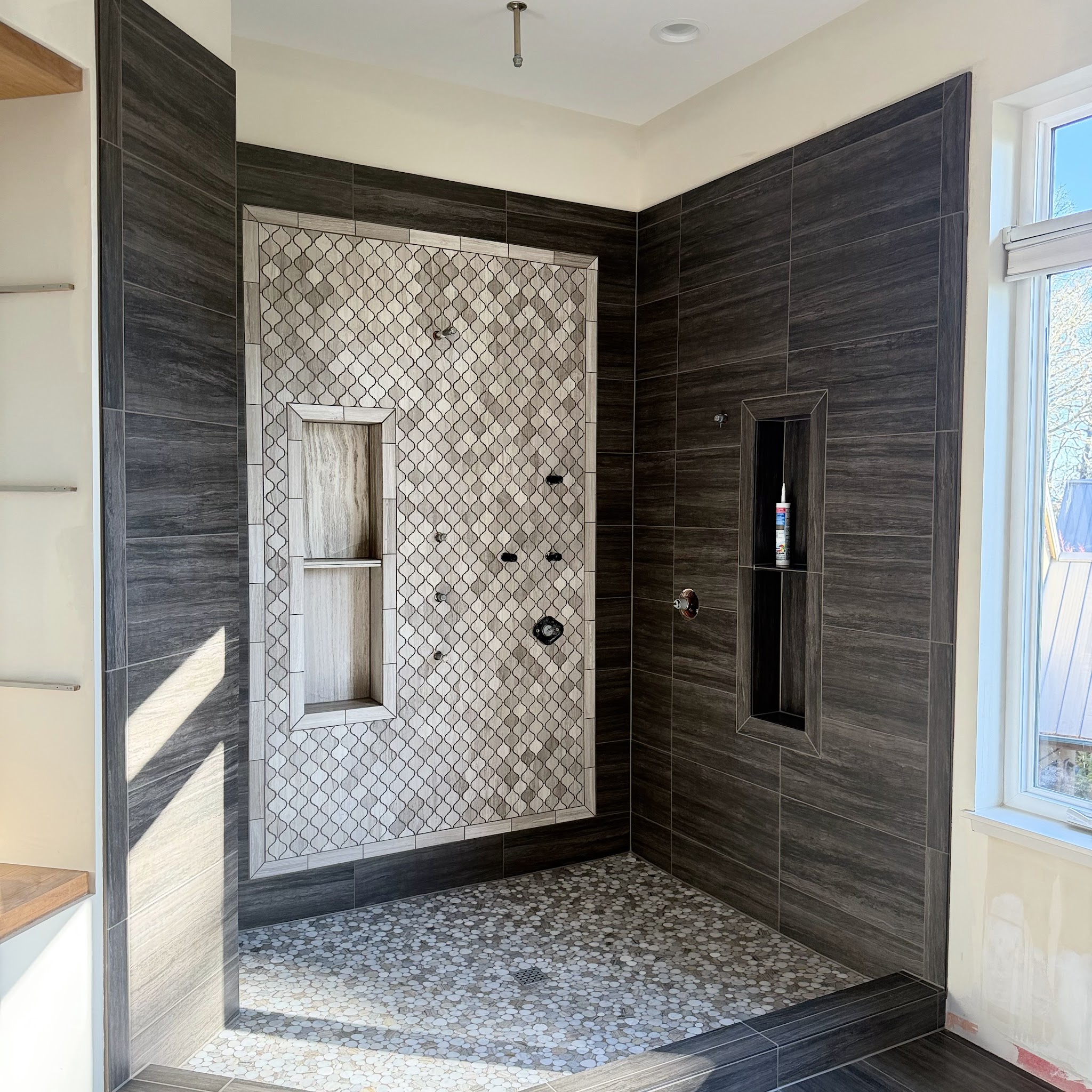 Custom tile shower with dark arabesque mosaic accent wall and frameless glass by Castor's Flooring