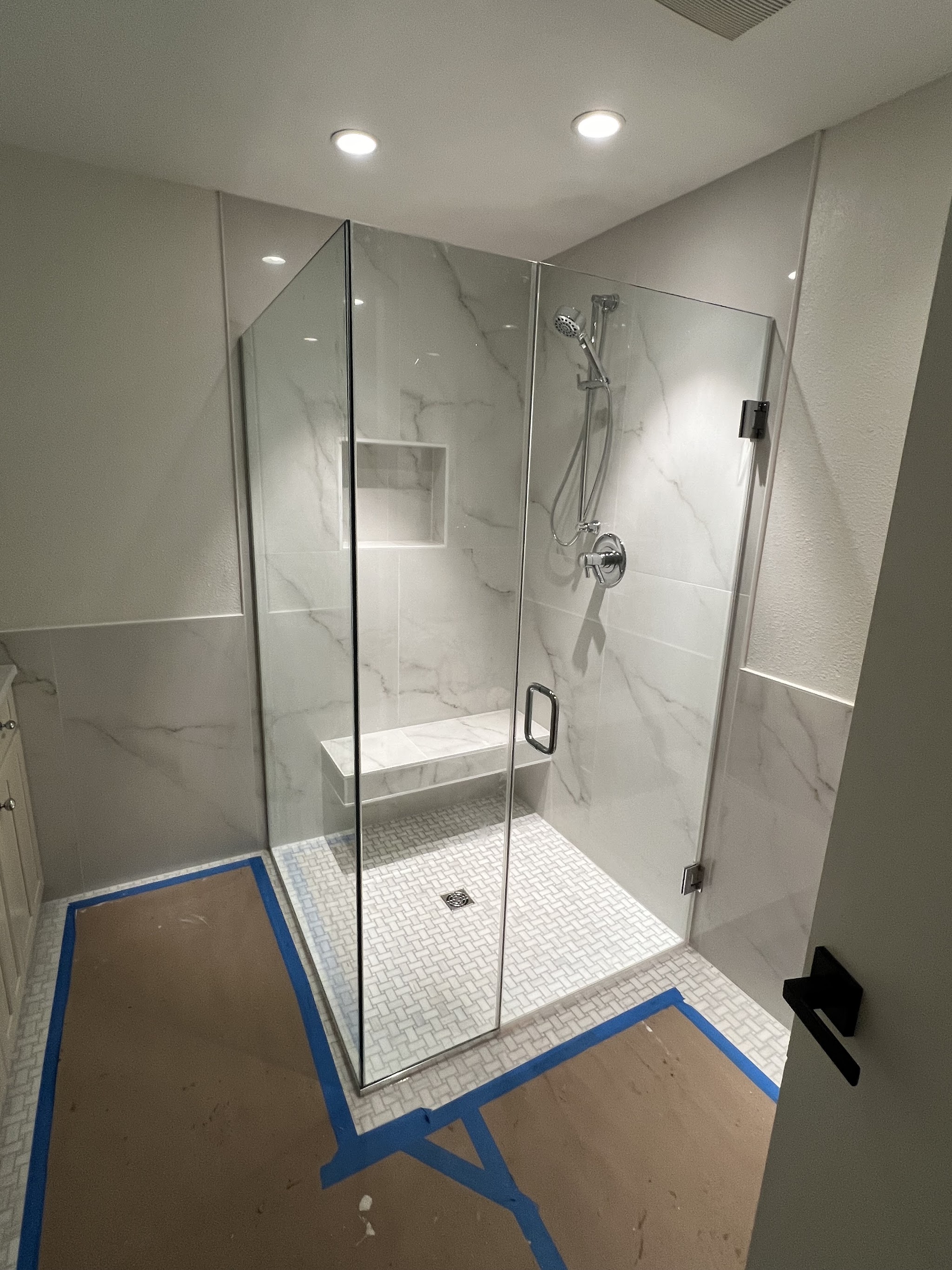 Frameless glass shower with marble-look tile and built-in bench by Castor's Flooring
